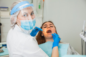 Female dentist curing teeth cavity in blue gloves and protective mask. Dentist caries treatment at...