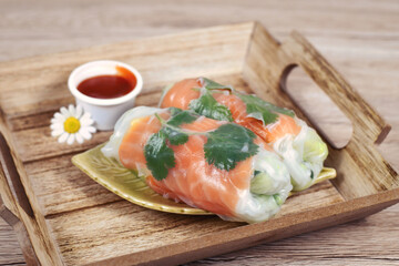 Traditional Vietnamese spring rolls filled with salmon, avocado,  salad and rice noodles on wooden tray