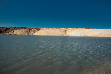 Small waves on blue water and a sandy beach. Pond on a sand quarry.