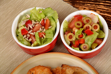 green lettuce with tomatoes and green olives next to fried potatoes and breaded cutlets