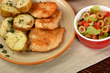 green lettuce with tomatoes and green olives next to fried potatoes and breaded cutlets
