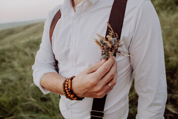 wedding boutonniere attached to the shirt, the groom in suspenders, boho style, close-up, a small bouquet of artificial flowers