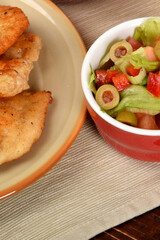 green lettuce with tomatoes and green olives next to fried potatoes and breaded cutlets