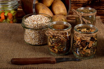 barley, spices in glass jars next to dried mushrooms and raw potatoes on a wooden brown table