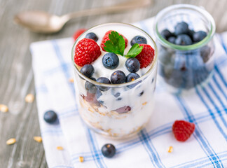 White yogurt in glass jar with fruits on grey background.