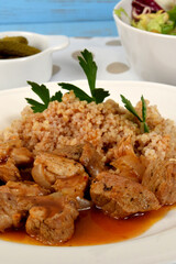 beef stew with onions and barleypieces of fried meat with onions and millet on a white plate next to lettuce