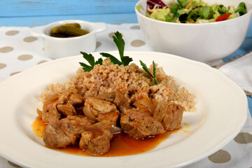 beef stew with onions and barleypieces of fried meat with onions and millet on a white plate next to lettuce