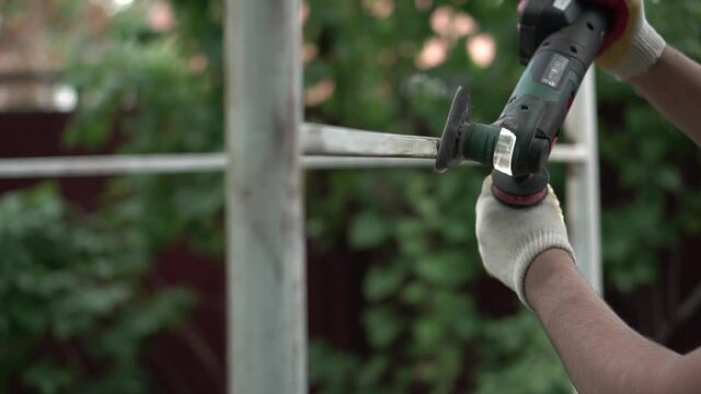 Man sanding metal beam and removing rust with multitool before painting