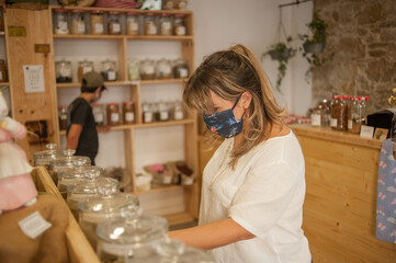 Caucasian woman in local store using mask and mantaining social distance bying daily products.
