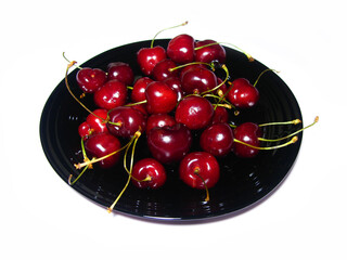 A handful of red cherries on a black plate on a white background. The view from the top.