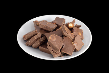 
Pieces of milk shekolada with hazelnuts on a saucer isolated on black background