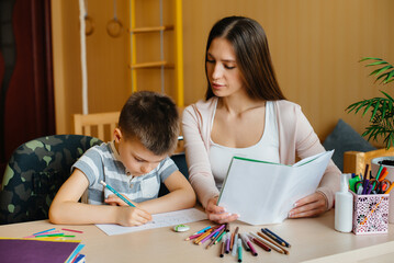 A young mother is doing homework with her son at home. Parents and training