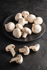 Champignon mushrooms healthy food on black plate on dark black textured background, angle view