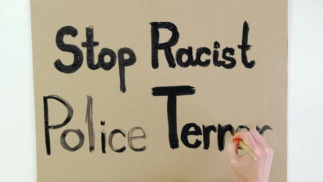 timelapse. close-up, hand writes slogan - Stop Racist Police Terror - with brush, using black paint on cardboard banner. Fighting against racism, for equal rights in USA.