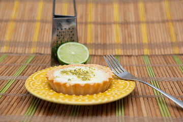 Side view of lemon tart on dish plate with lemon slices on table.
