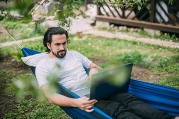 A man works with a laptop in a hammock in a country house