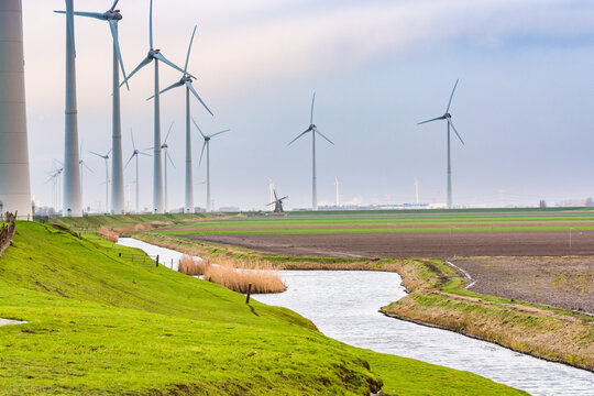 Wind electricity with water channel and old wind mill in background between new technology on the north of Netherlands near Eemshaven