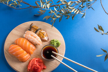 Delicious appetizing nigiri sushi set served on wooden plates with soy sauce and chopsticks. Flat lay on blue background