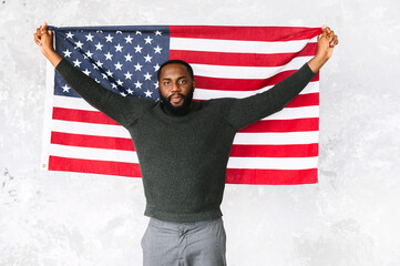 Black young guy raised his hands up with US flag, he looks calm and smiles. Studio shot