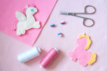 Pegasus toy, unicorn toy, scissors, thread and buttons on a felt background. Handmade pink flat lay. Sewing fairy ponies.