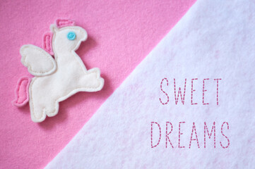 Handmade toy Pegasus on a pink felt background. Sewn inscription Sweet dreams. Handmade pink flat lay. Sewing funny felt pony with wings for a daughter.