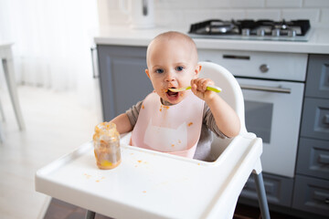baby sits in a feeding chairgirl in the kitchen and eats