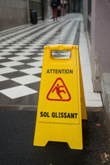 Closeup of wet floor sign on yellow plastic board , with text in french, attention sol glissant,...