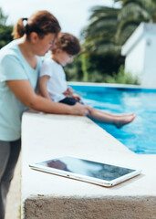 Mother and son playing in the pool with digital tablet.