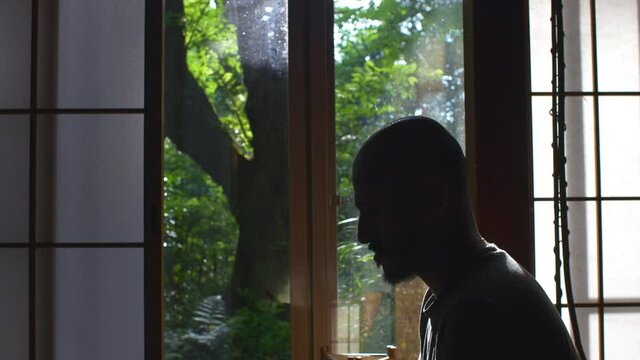 Silhouette Side View Of Adult Male Sitting And Meditating Indoors. Locked Off