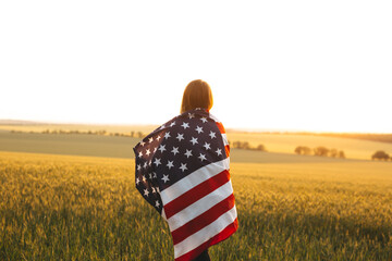 Young girl with the American flag in a wheat field at sunset. 4th of July.  Independence Day.