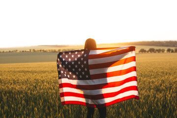 Young girl with the American flag in a wheat field at sunset. 4th of July.  Independence Day.