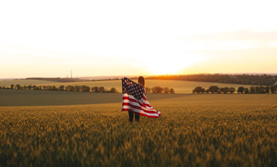 Beautiful girl with American flag in a wheat field at sunset. 4th of July.  Independence Day, Patriotic holiday.