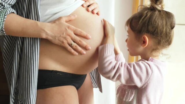 little girl older sister touching pregnancy belly, smiling looking at camera