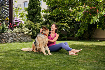 Obraz premium Young attractive fit yogi brunette playing with her dog in backyard.