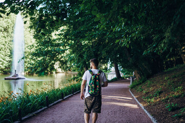 Fototapeta na wymiar Sofia Park, Uman. A man with a backpack walks along the lake embankment. Man turned his back on the background of the lake with a tall beautiful fountain