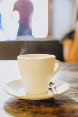 White cup with saucer and small spoon on a wooden table. Hot espresso in a white cup. Delicious coffee for breakfast in a cafe.