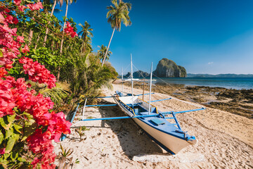 El Nido, Palawan, Philippines. Native banca boat and vibrant flowers at Las cabanas beach with...