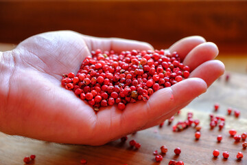 Pink peppercorns in a man's hand on a wooden background. Seasoning in the palm of a person. The concept of delicious food.