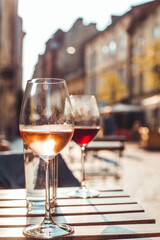 Glass of rose wine at the table of restaurant located on the streets of old city of Lviv. Glass of red wine in the background and some old houses during sunset in summer.