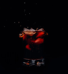 Glass of whiskey isolated on black background with ice falling into the beverage.  Splashes of drink around. 