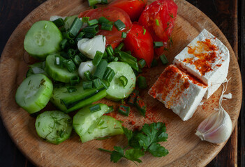 Rustic salad, from tomatoes, cucumbers, cheese, garlic on a wooden board.