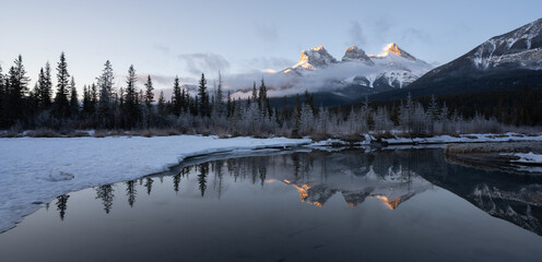 Panoramic winter sunrise shot from Canadian Rockies with mountain reflected in water, shot at Three Sisters Mountain, Canmore, Alberta, Canada