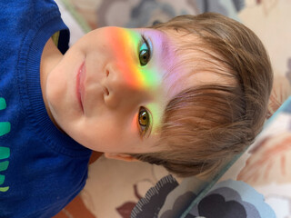 A baby boy with light rainbow on his face during Covid-19 quarantine at home. Stay at home Social media campaign for coronavirus prevention, hope during coronavirus pandemic concept.
