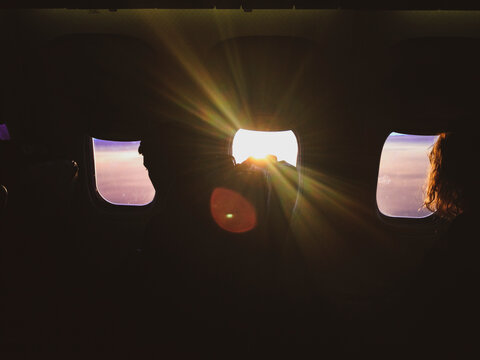 Silhouette of people looking through the airplane windows during flight with the sun shinning. Abstract concept.