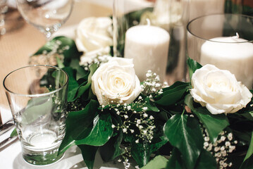 Festive table floral decoration. White roses and white candles on wooden table. Celebration, birthday and wedding concept.