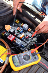 A mechanic/service engineer checking the fuse box of a car with a voltmeter 