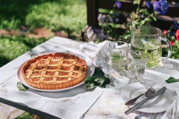 Apple rhubarb pie and herbal tea on a set table in the garden on a sunny summer day.