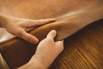 close up hands of a man working with brown leather on the table