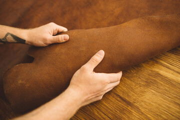 close up hands of a man working with brown leather on the table