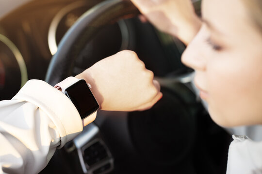 Close up woman looking on hand with smart watch, empty screen, sitting in car as driver, holding steering wheel. Hurry for work, online application, notification or message on technology device